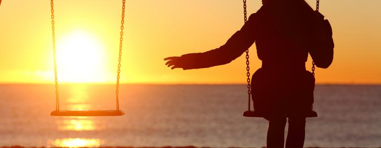 Femme assise sur une balançoire à côté d'une autre balançoire vide devant un coucher de soleil.